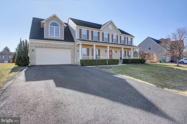 colonial home featuring a porch, a garage, a front lawn, and aphalt driveway