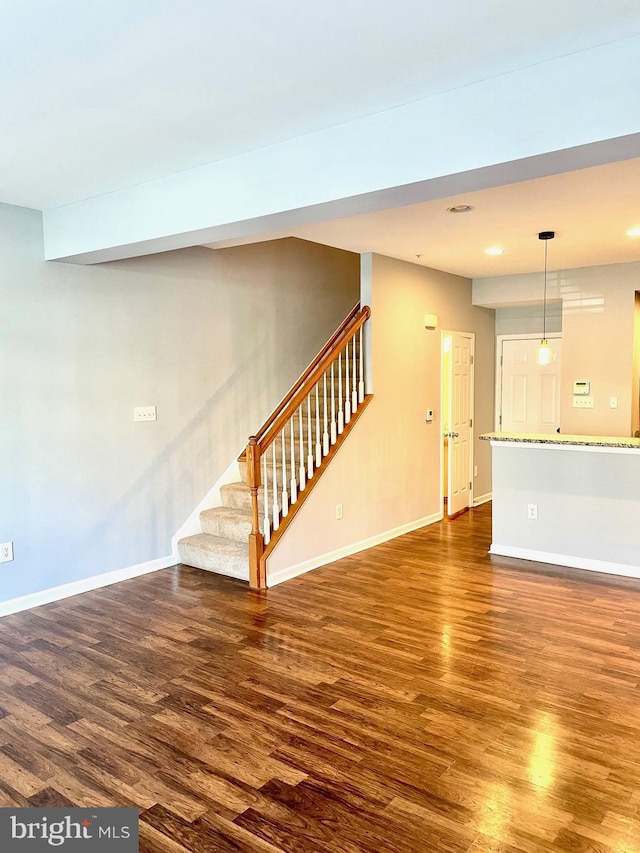 unfurnished living room featuring dark wood-style floors, baseboards, and stairs