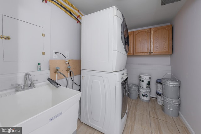 laundry area featuring light tile patterned floors, stacked washer / dryer, cabinet space, and a sink