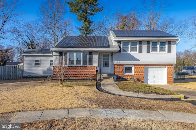 tri-level home featuring fence, a front yard, a garage, brick siding, and solar panels