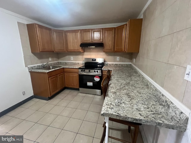 kitchen featuring light tile patterned floors, under cabinet range hood, electric range, a sink, and brown cabinets