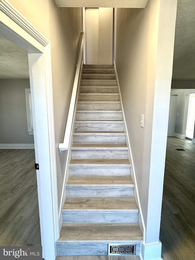 staircase with visible vents, baseboards, and wood finished floors