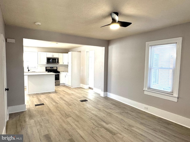 kitchen with baseboards, stainless steel appliances, white cabinetry, and light wood-style floors