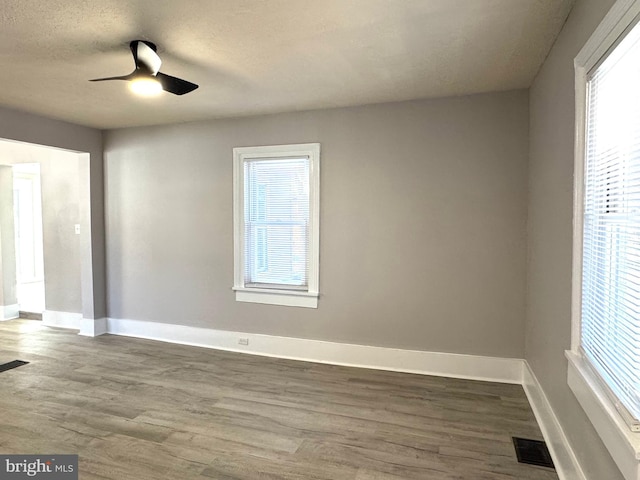 unfurnished room with a wealth of natural light, visible vents, and dark wood-type flooring