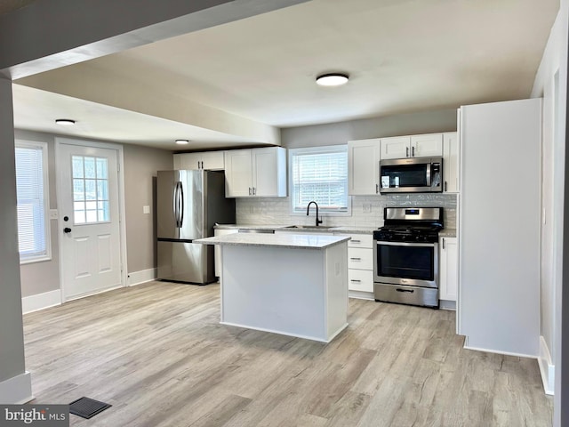 kitchen with backsplash, light wood-style flooring, appliances with stainless steel finishes, a sink, and a kitchen island