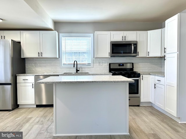 kitchen with light wood finished floors, white cabinetry, stainless steel appliances, and a sink