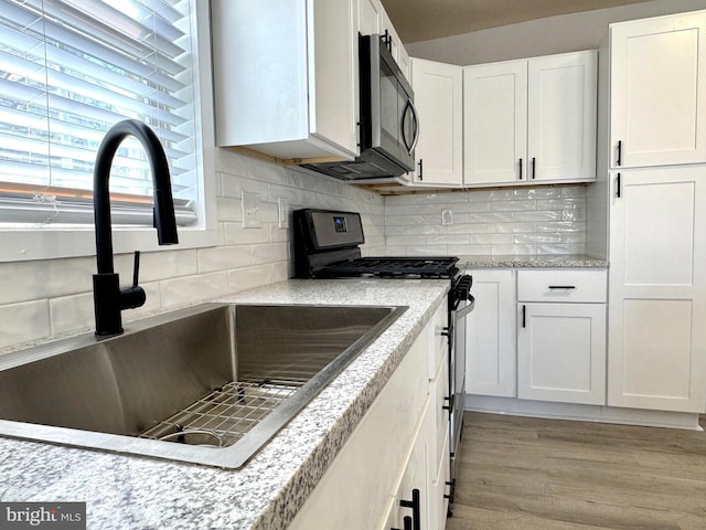 kitchen with a sink, white cabinetry, light wood-type flooring, backsplash, and gas stove