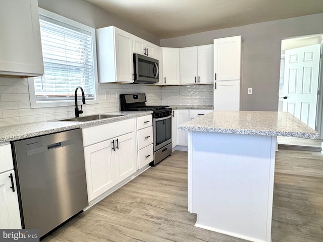 kitchen with white cabinets, a kitchen island, stainless steel appliances, light wood-style floors, and a sink