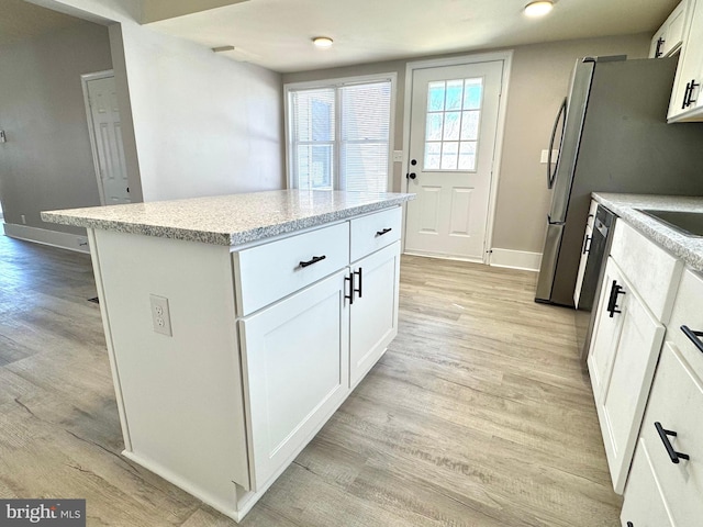 kitchen with light wood-type flooring, white cabinets, a kitchen island, and baseboards