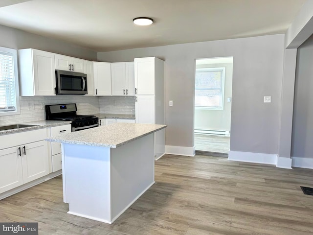 kitchen featuring light wood finished floors, tasteful backsplash, baseboard heating, stainless steel appliances, and white cabinetry