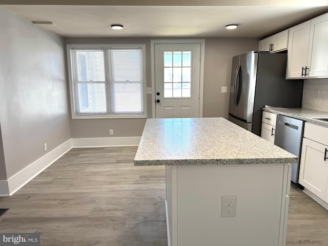 kitchen with appliances with stainless steel finishes, white cabinetry, a kitchen island, light wood-type flooring, and baseboards