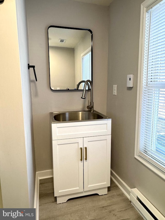 bathroom with baseboards, a baseboard radiator, vanity, and a healthy amount of sunlight