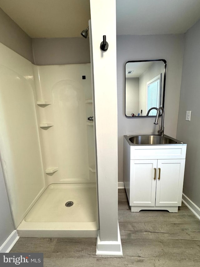 bathroom featuring wood finished floors, a shower stall, vanity, and baseboards