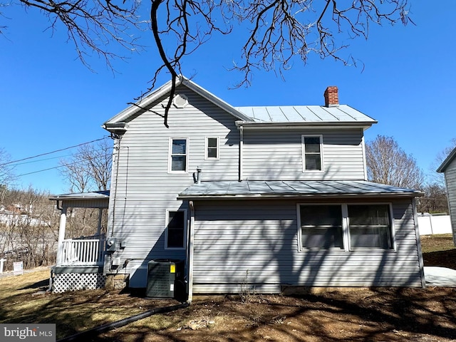 back of house featuring metal roof, a standing seam roof, a chimney, and cooling unit