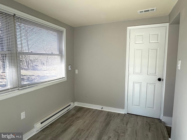 empty room with dark wood-style floors, baseboard heating, visible vents, and baseboards