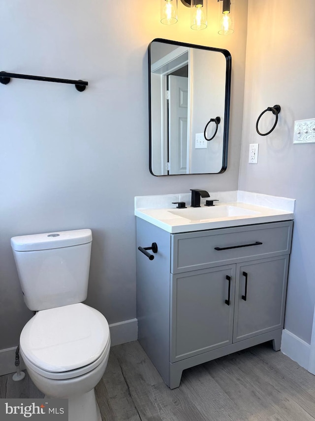 bathroom featuring toilet, baseboards, wood finished floors, and vanity