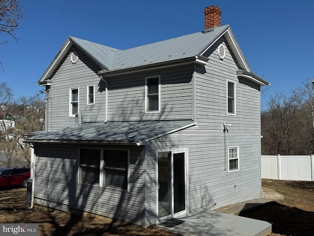 rear view of house featuring metal roof, a chimney, and fence