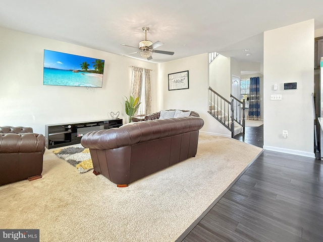 living area featuring stairs, dark wood-type flooring, baseboards, and ceiling fan