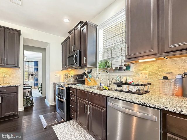 kitchen with dark brown cabinetry, dark wood finished floors, decorative backsplash, stainless steel appliances, and a sink