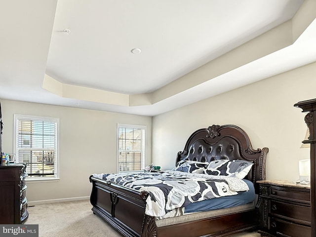 bedroom with baseboards, a raised ceiling, and light colored carpet