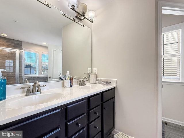 bathroom with double vanity, an enclosed shower, baseboards, and a sink