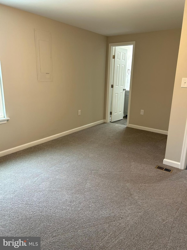 spare room featuring electric panel, carpet flooring, baseboards, and visible vents