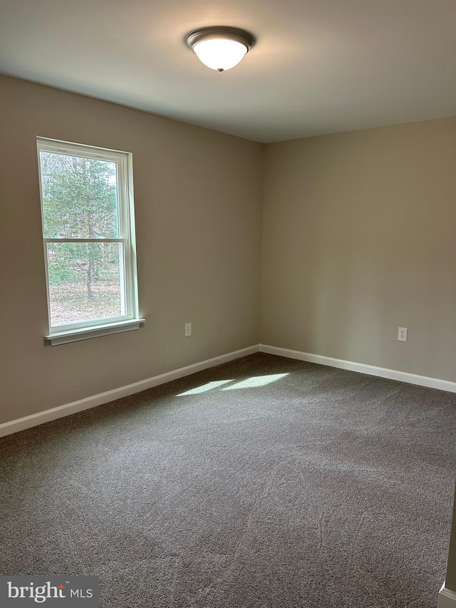 spare room with baseboards and dark carpet