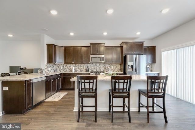 kitchen with dark brown cabinetry, wood finished floors, a kitchen island, and stainless steel appliances