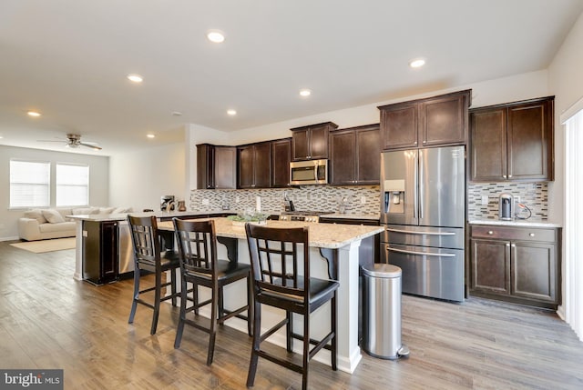 kitchen with dark brown cabinetry, a kitchen breakfast bar, appliances with stainless steel finishes, and light wood-style floors