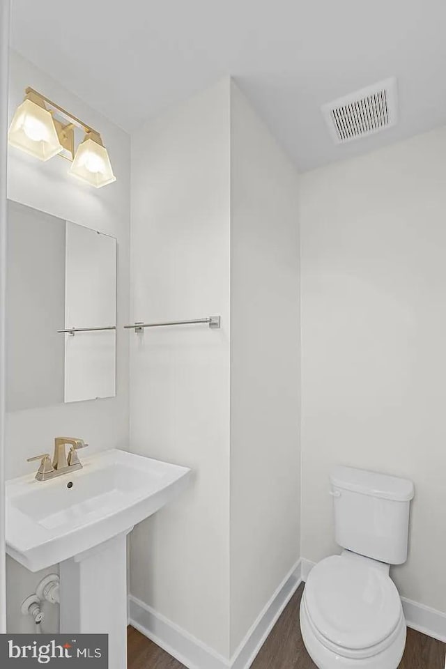 half bath with visible vents, toilet, baseboards, and wood finished floors