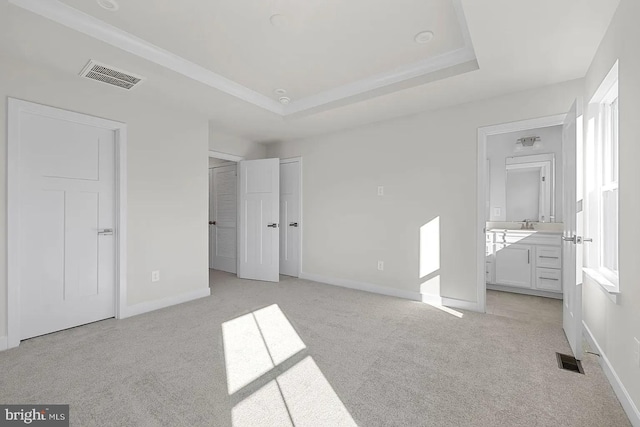 unfurnished bedroom featuring a tray ceiling, visible vents, baseboards, and light colored carpet