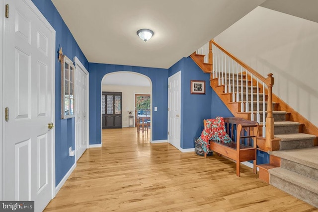 entrance foyer featuring baseboards, stairs, arched walkways, and wood finished floors