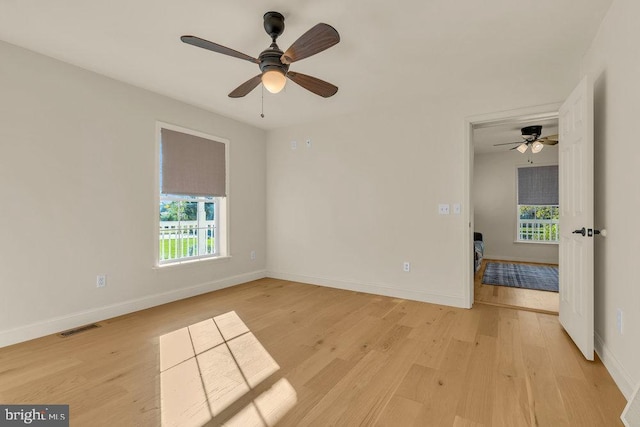 spare room featuring light wood-style floors, a wealth of natural light, visible vents, and baseboards