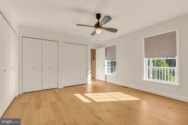 unfurnished bedroom with light wood finished floors, two closets, visible vents, and baseboards