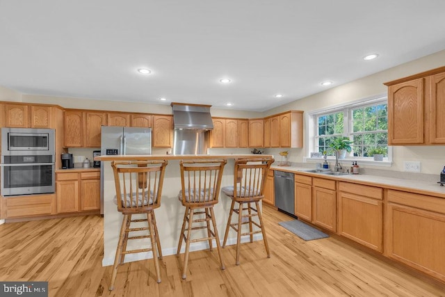 kitchen with stainless steel appliances, a breakfast bar, wall chimney range hood, light wood-type flooring, and a center island