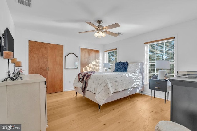 bedroom featuring visible vents, ceiling fan, light wood finished floors, and two closets