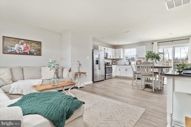 living area with light wood-style flooring, visible vents, and baseboards