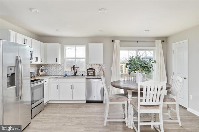 kitchen featuring stainless steel appliances, backsplash, white cabinets, a sink, and light wood-type flooring