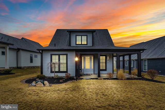 view of front of home with a shingled roof, a front yard, and covered porch