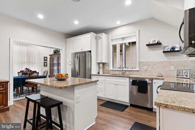 kitchen featuring a center island, stainless steel appliances, white cabinets, a sink, and wood finished floors