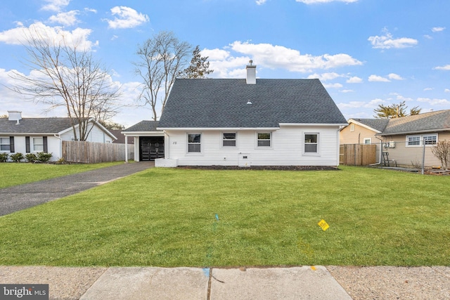 rear view of property featuring aphalt driveway, roof with shingles, a chimney, a lawn, and fence