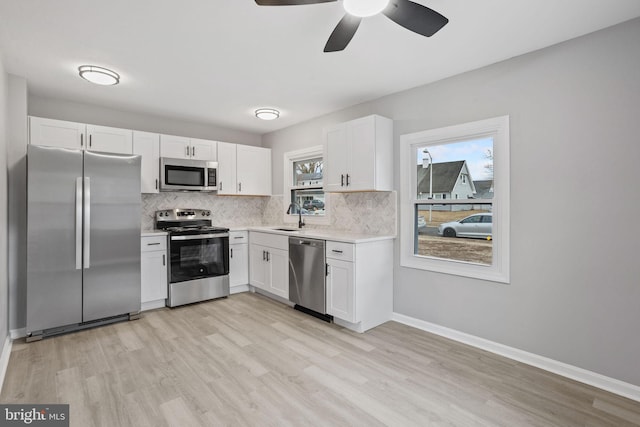 kitchen with stainless steel appliances, light countertops, backsplash, white cabinets, and a sink