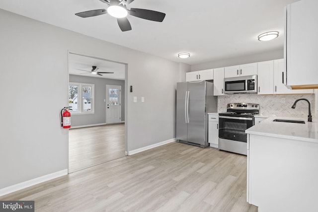 kitchen featuring stainless steel appliances, a sink, light wood-style floors, light countertops, and decorative backsplash