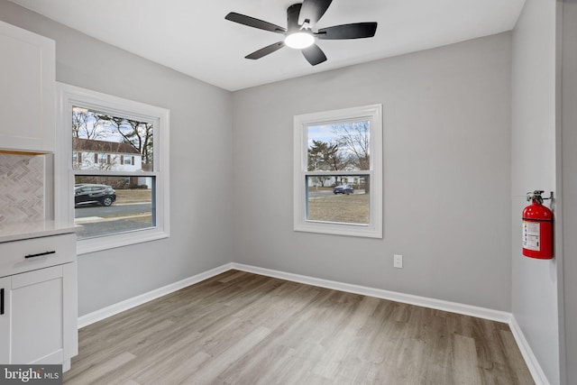 unfurnished room with light wood-type flooring, plenty of natural light, a ceiling fan, and baseboards