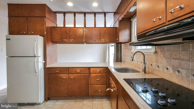 kitchen with brown cabinetry, freestanding refrigerator, a sink, black electric cooktop, and backsplash