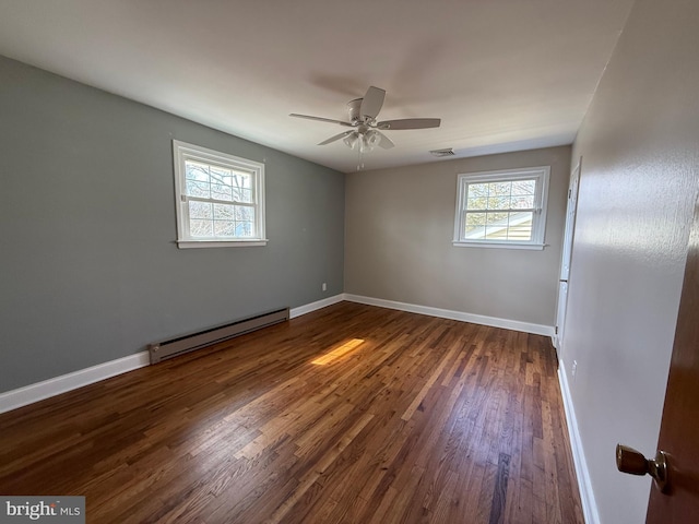 empty room featuring a wealth of natural light, baseboards, baseboard heating, and dark wood-style flooring