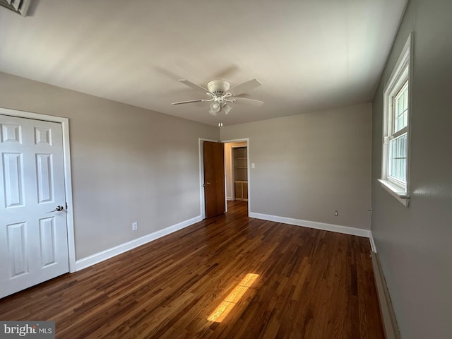 unfurnished bedroom with baseboard heating, ceiling fan, dark wood-type flooring, and baseboards