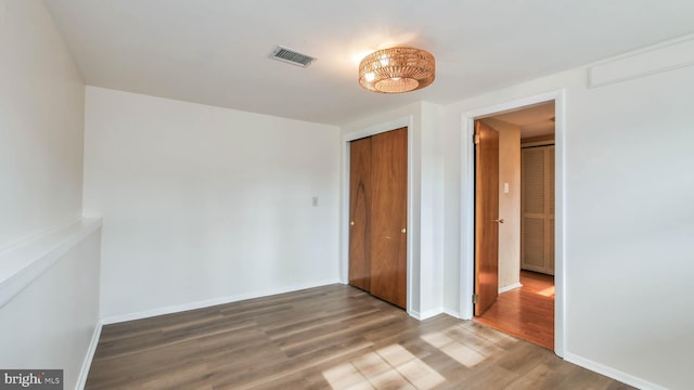 unfurnished bedroom featuring a closet, visible vents, baseboards, and wood finished floors