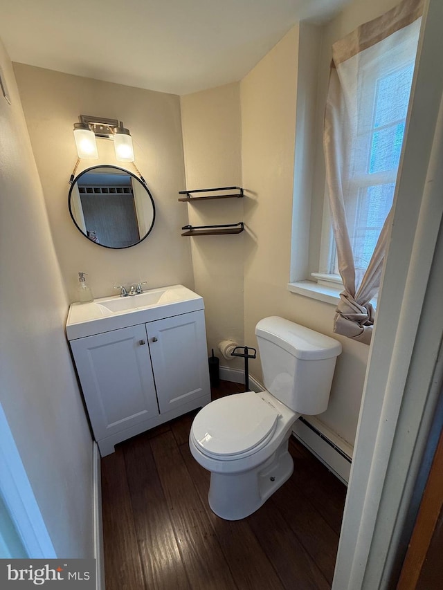 half bathroom with toilet, wood finished floors, vanity, and a baseboard radiator