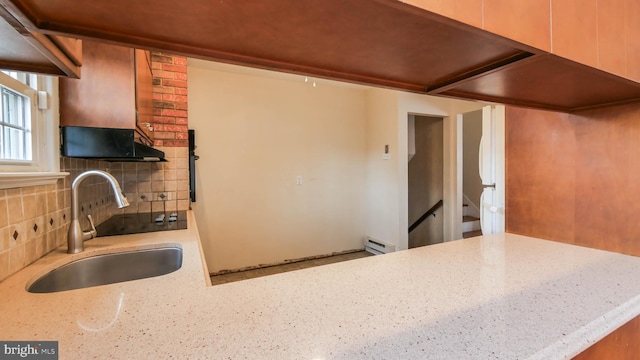 kitchen featuring tasteful backsplash, a sink, light stone countertops, under cabinet range hood, and a baseboard radiator